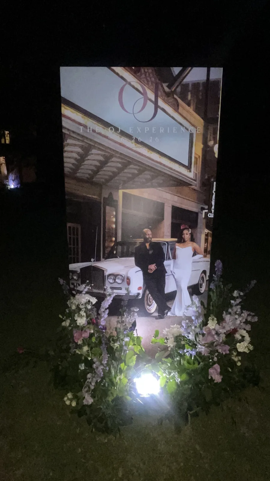 A custom photo board lit at night beside the couple's car outside the venue