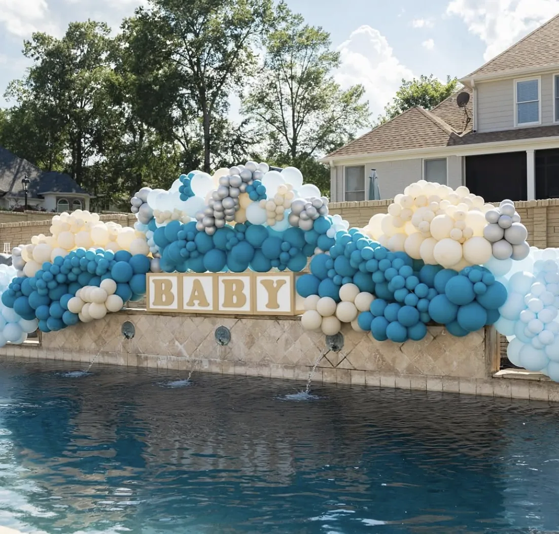 A blue and white baby shower balloon garland and 'Baby' sign beside a pool