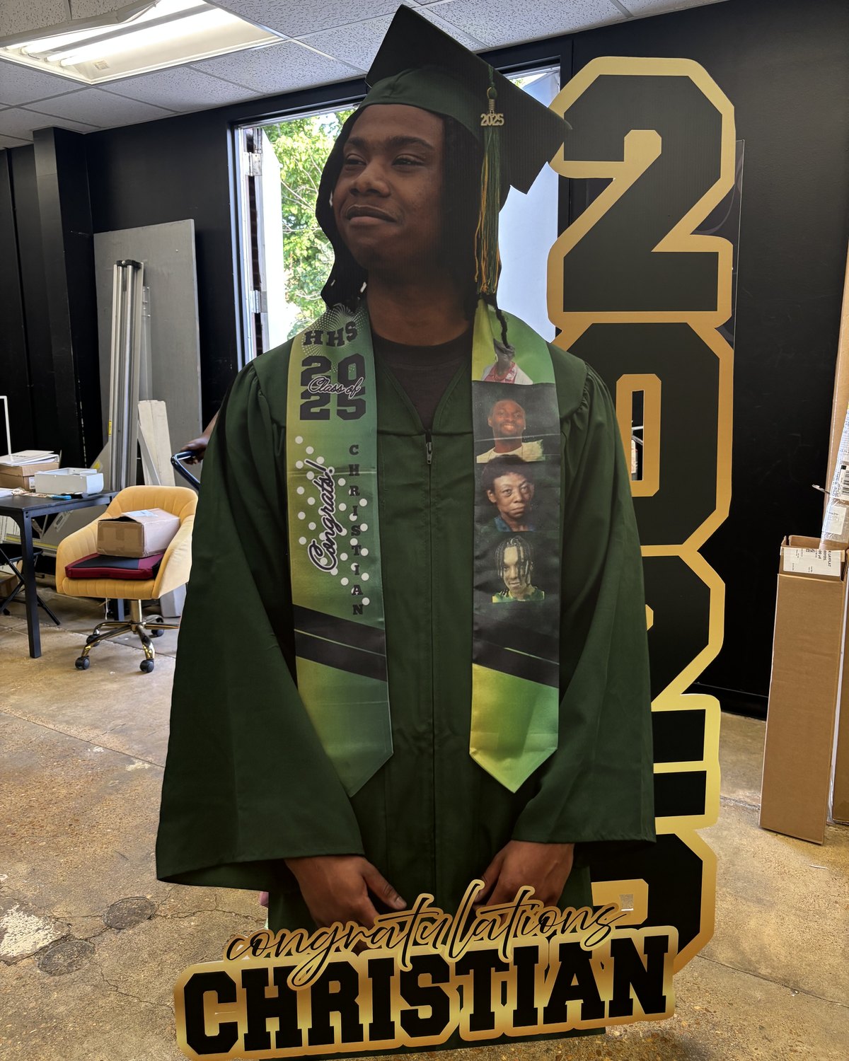 A life-size cutout of a graduate in a green cap and gown on a Congratulations Christian base
