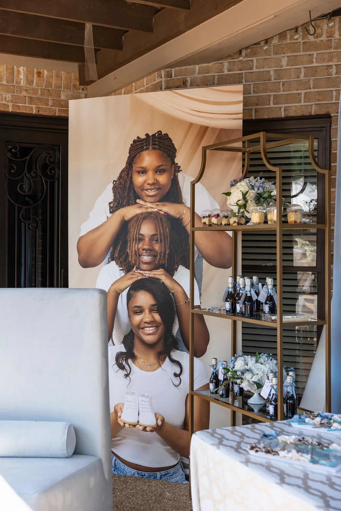 A tall custom photo board of three smiling women holding baby shoes at a baby shower