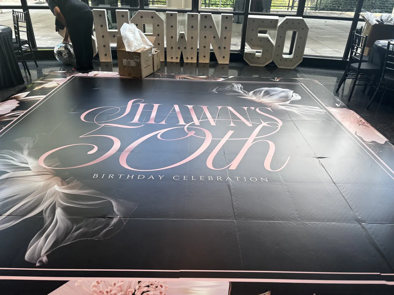 A black dance floor wrap with pink script for a 50th birthday celebration