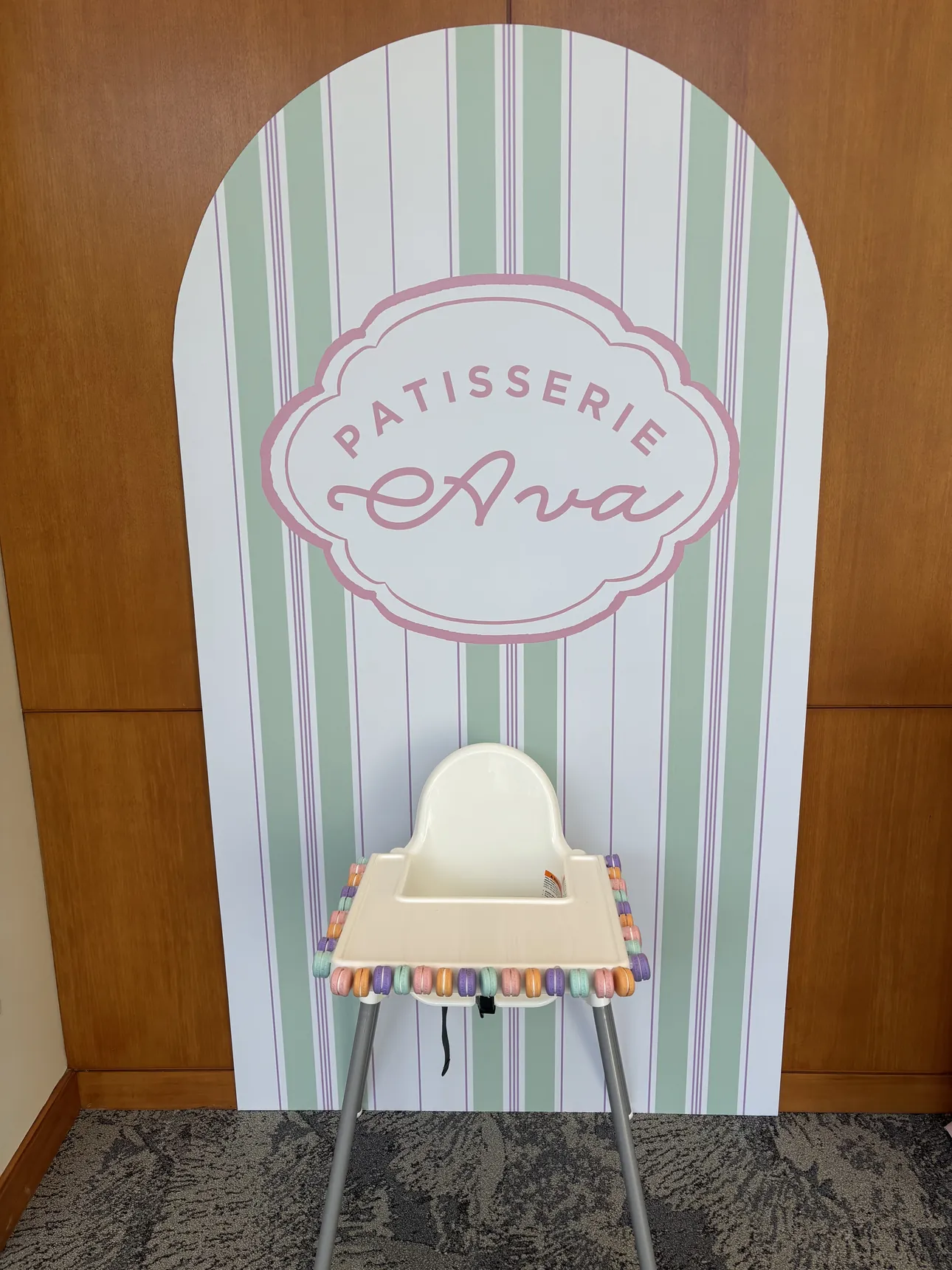 A striped Patisserie Ava arch backdrop behind a high chair for a first birthday