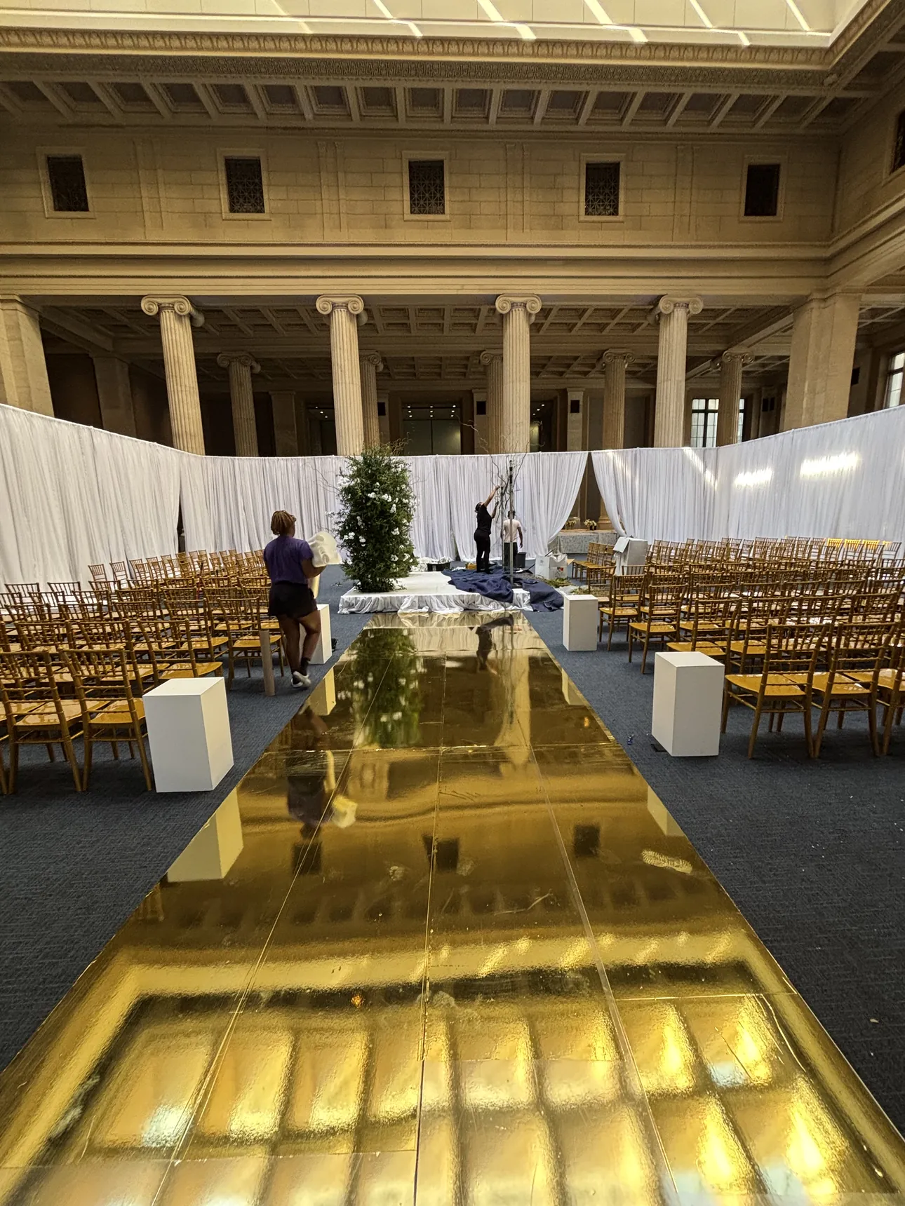 A gold aisle runner through a pillared hall set for a ceremony