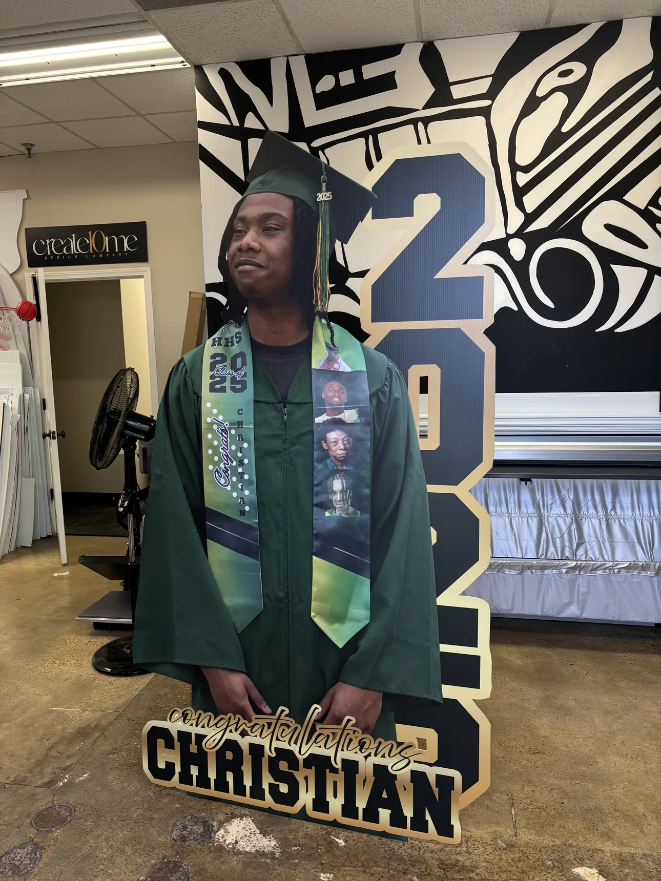 A life-size cutout of a graduate in a green cap and gown with a Congratulations Christian base