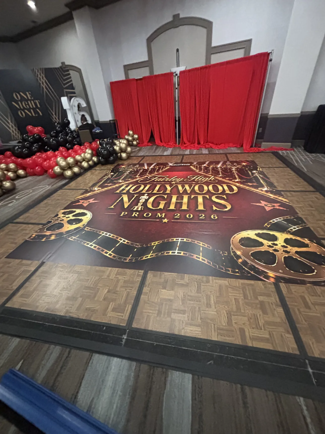 A Fairley High Hollywood Nights Prom 2026 dance floor wrap with gold film reels, laid in front of red drapes